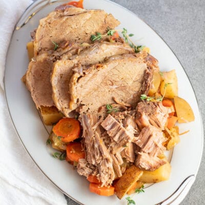 Sliced slow cooker eye of round roast on white serving plate with veggies.