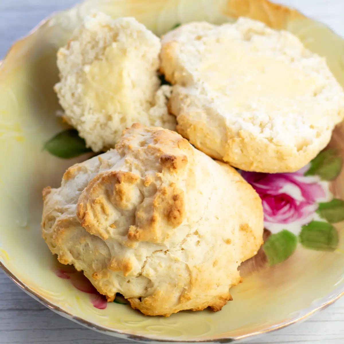 Best 3 ingredient drop biscuits on vintage floral plate with one cut and buttered in background.