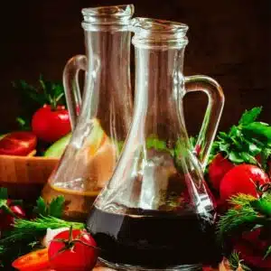 Square image of balsamic vinegar on a table with fresh produce.