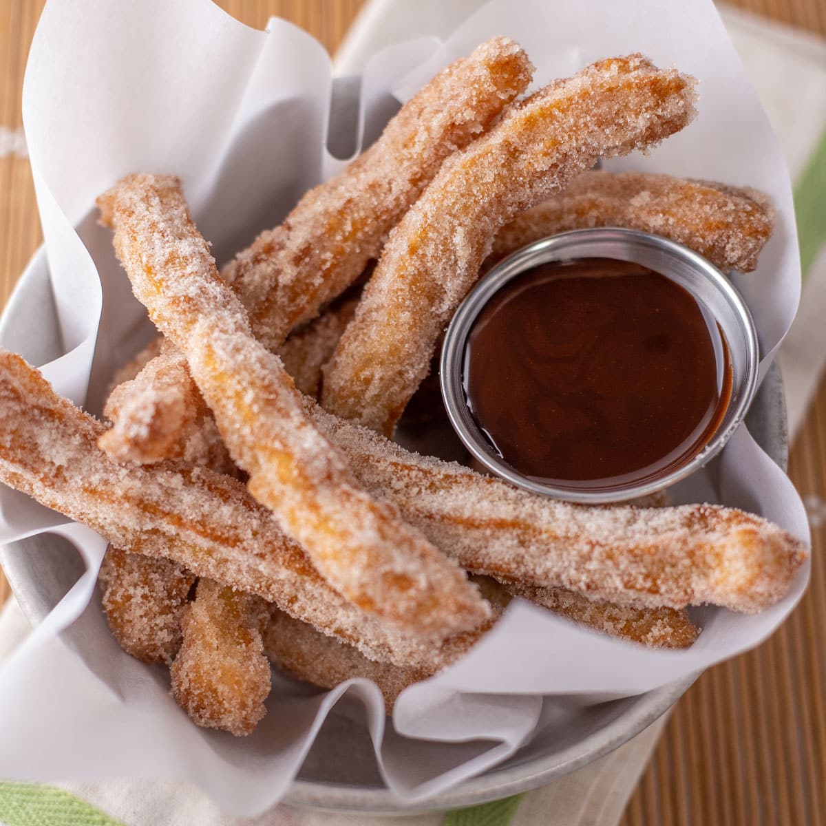 Homemade churros with cinnamon sugar coating and chocolate dipping sauce in basket.