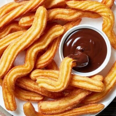 Crispy fried churros on white plate with chocolate dipping sauce.