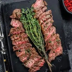 Tender pan seared hanger steak is sliced and served on dark surface with fresh thyme.