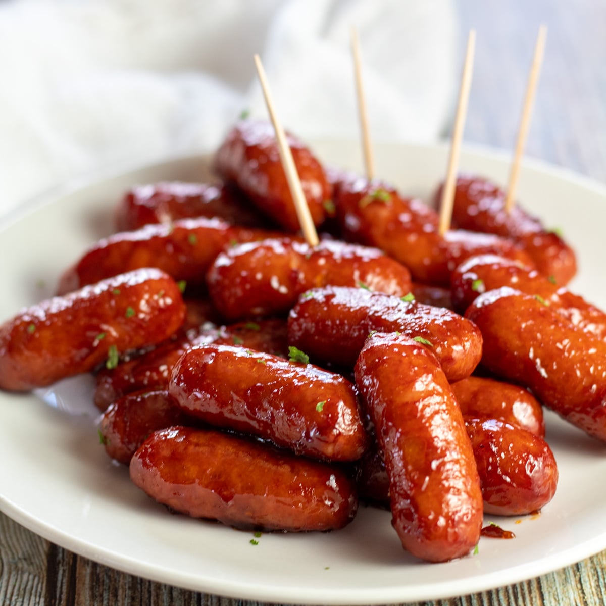 Square image of bbq little smokies on a white plate with toothpicks for easy serving.