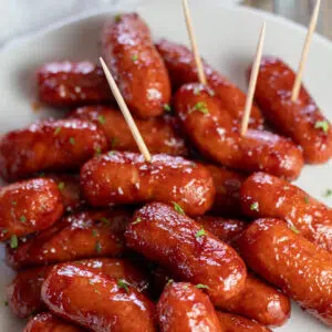 Close up square image of bbq little smokies on a white plate with toothpicks for easy serving.