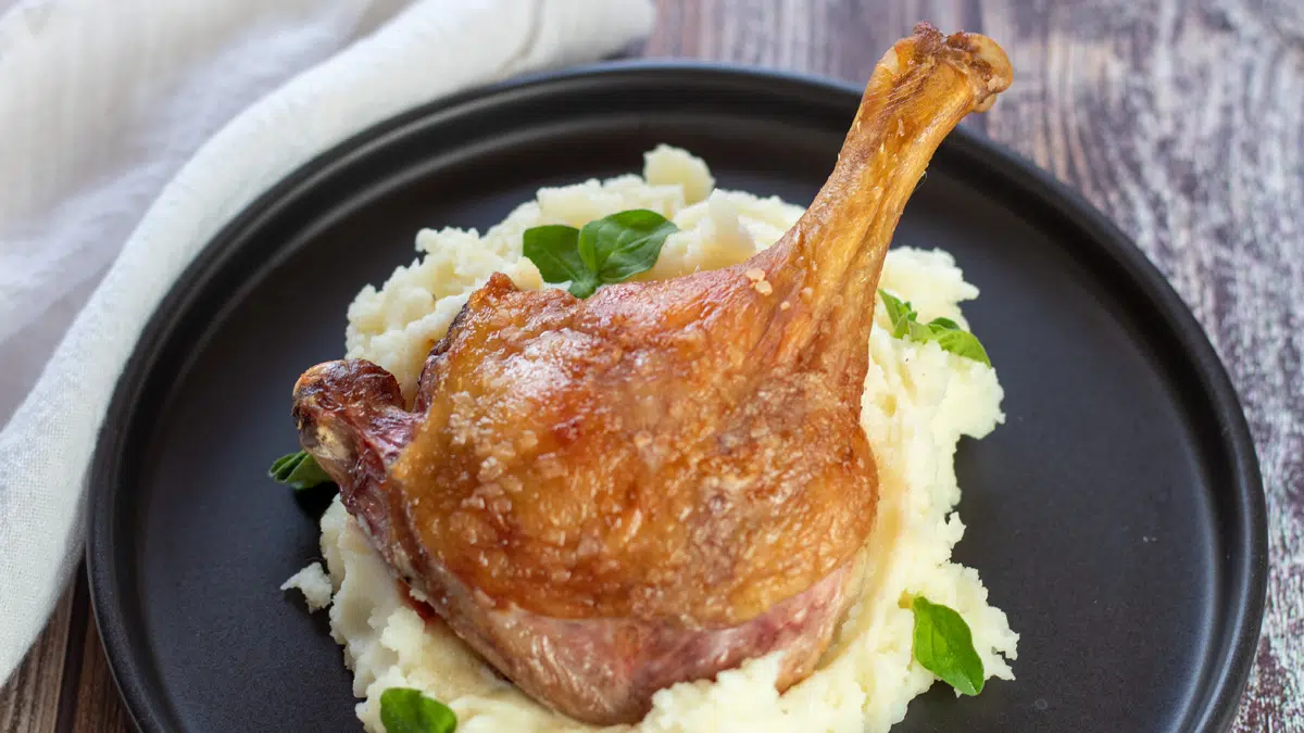 Wide image of a duck leg on a pile of mashed potatoes.