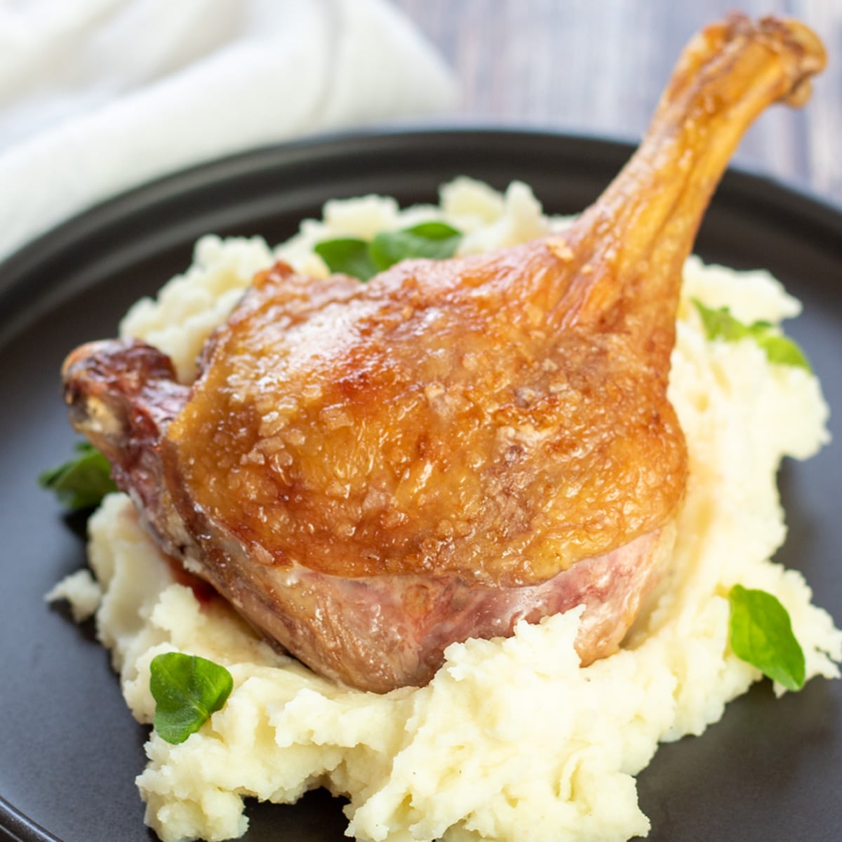 Square image of a duck leg on a pile of mashed potatoes.
