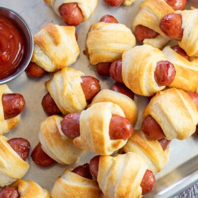 Square image of air fryer pigs in a blanket on a metal tray with ketchup.