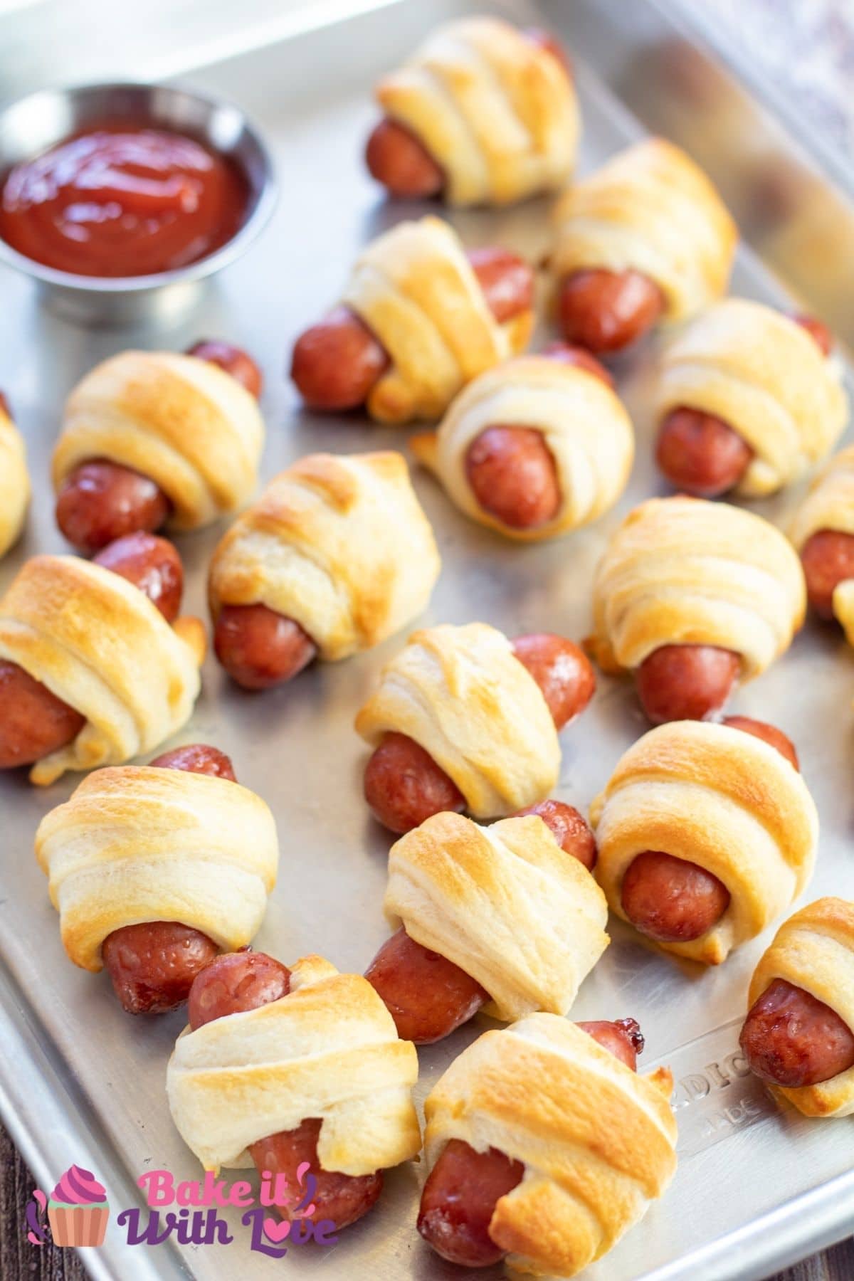 Tall image of air fryer pigs in a blanket on a metal tray with ketchup.