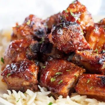 Wide image of baked bbq rib tips on a white plate served over rice.