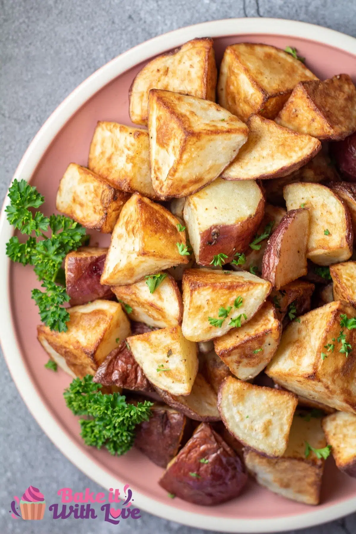 Tall overhead of the plated crispy roasted red potatoes with parsley garnish on dusty rose colored plate.