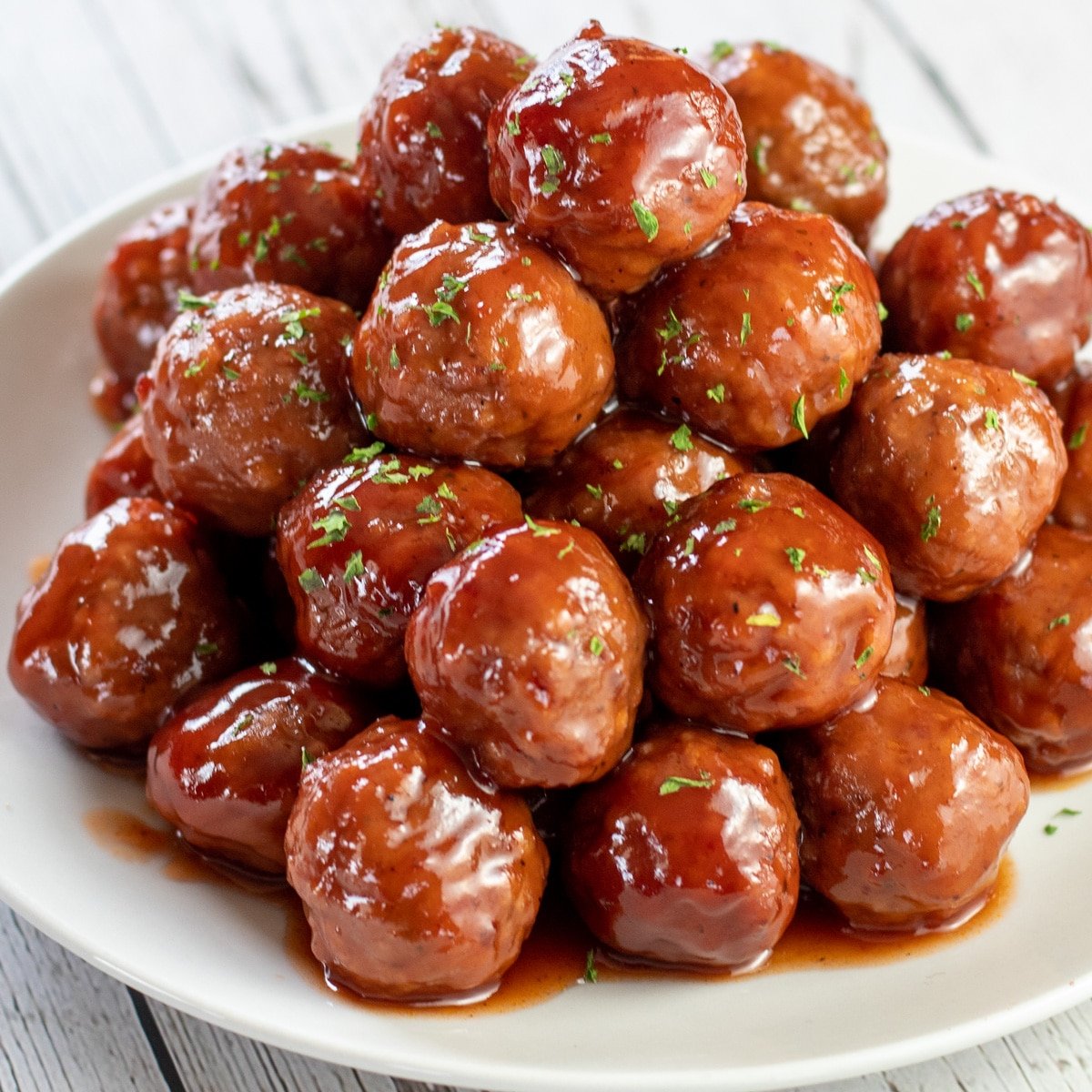 Square image of crockpot grape jelly meatballs piled up high on a white plate.