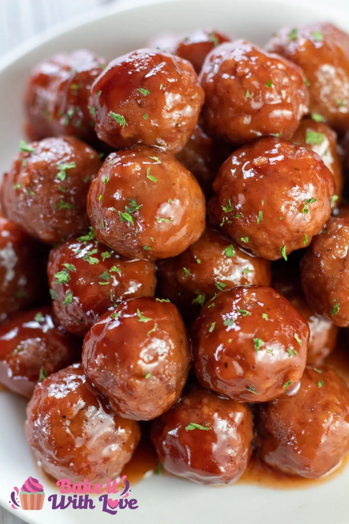 Tall image of crockpot grape jelly meatballs piled up high on a white plate.