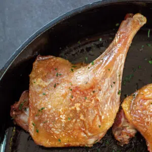 Square image of duck confit in a cast iron pan.