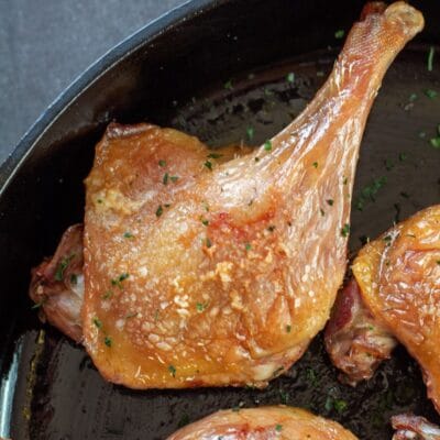 Tall image of duck confit in a cast iron pan.