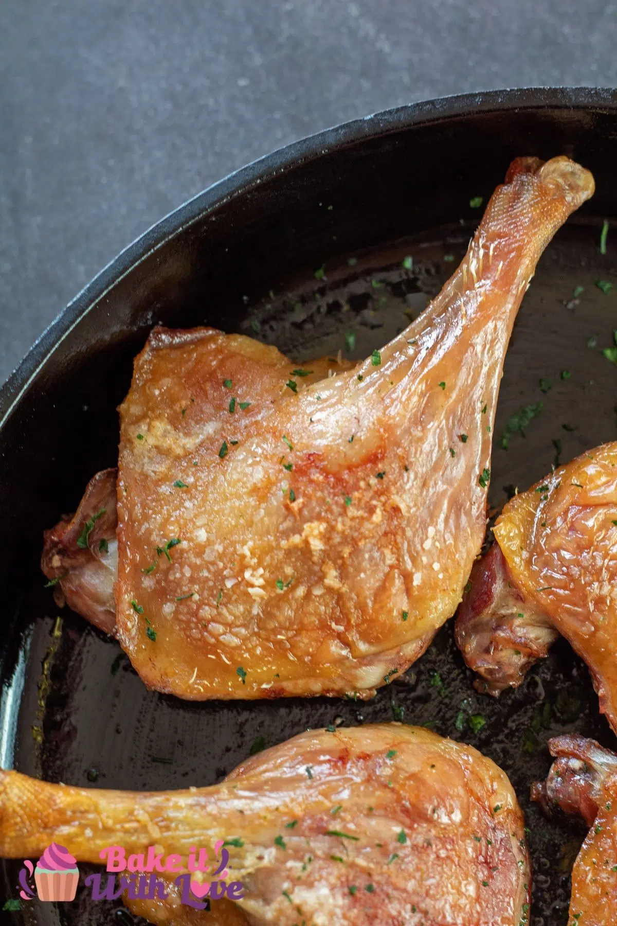 Tall image of duck confit in a cast iron pan.