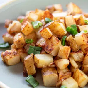 Square image of duck fat fried potatoes topped with green onion on a plate.