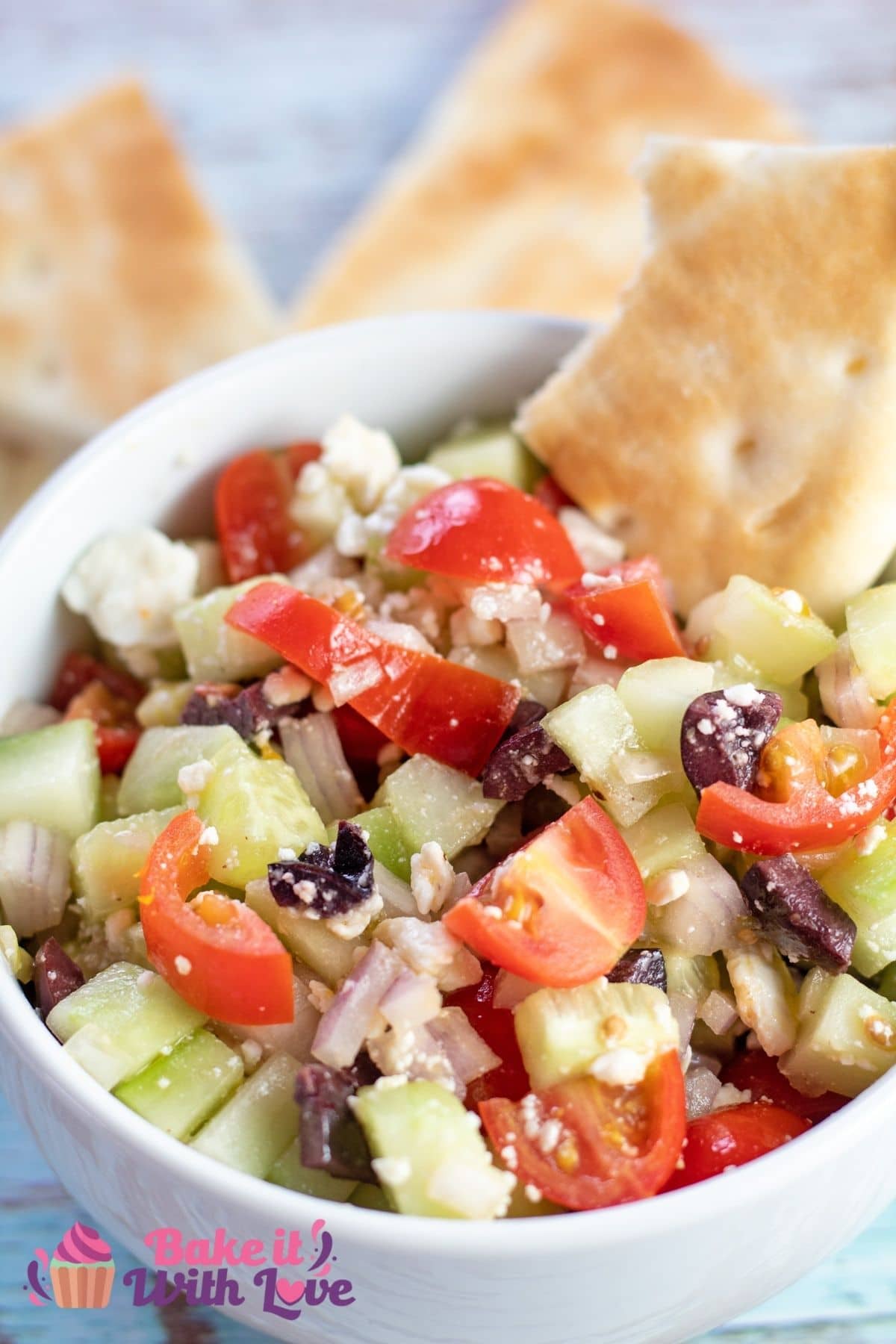Closeup on the dished Greek salad with pita bread being dipped into it.