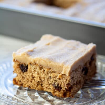 Square image of a slice of raisin cake on a glass plate.