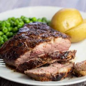 This crazy delicious pan seared lamb leg steak is sliced to serve with peas and boiled potatoes.