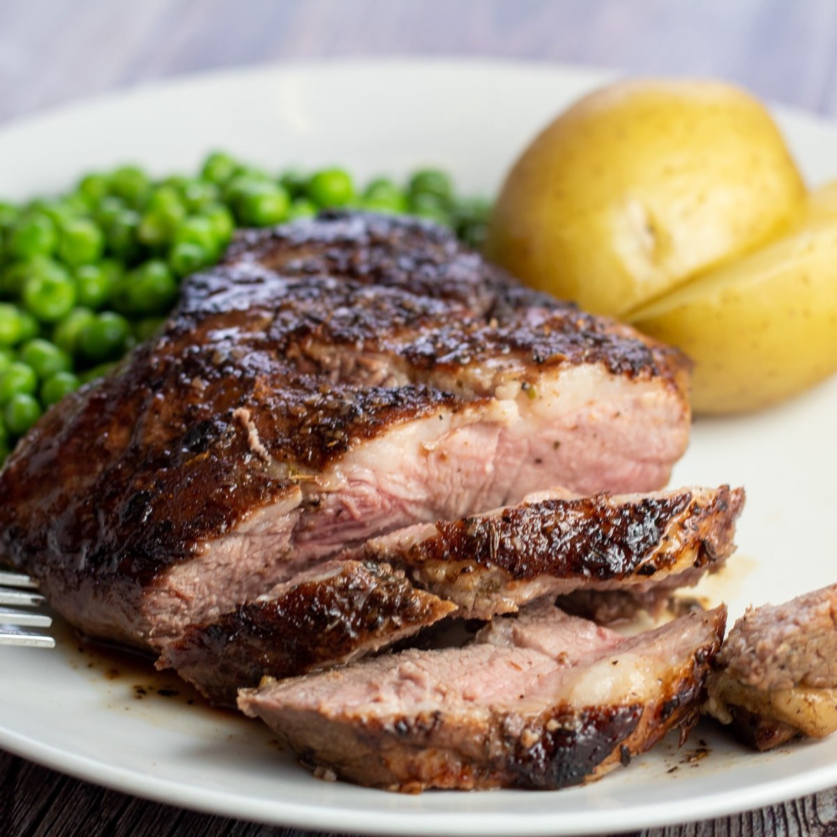 Ce délicieux steak de gigot d'agneau poêlé est coupé en tranches pour être servi avec des pois et des pommes de terre bouillies.