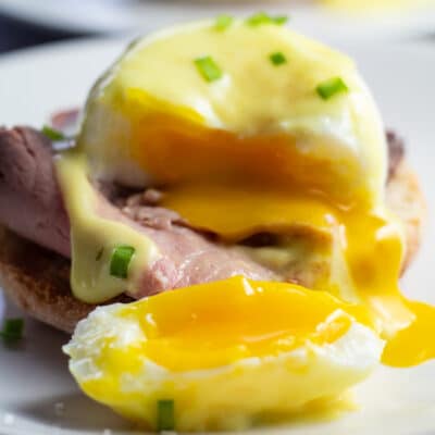 Богати и вкусни първокласни яйца Бенедикт се разцепват с течния жълтък в чинията.