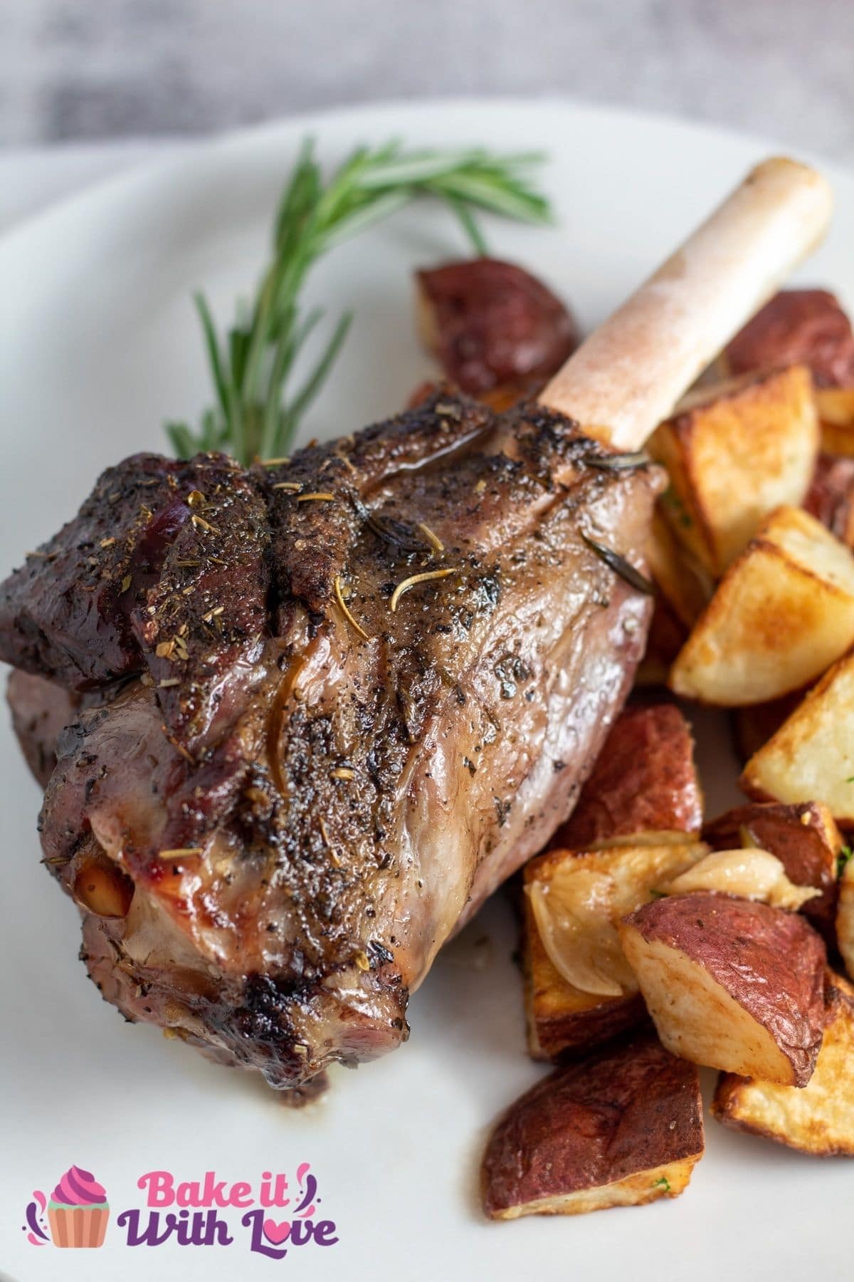 Tall image of roasted lamb shank on a white plate with roasted potatoes.