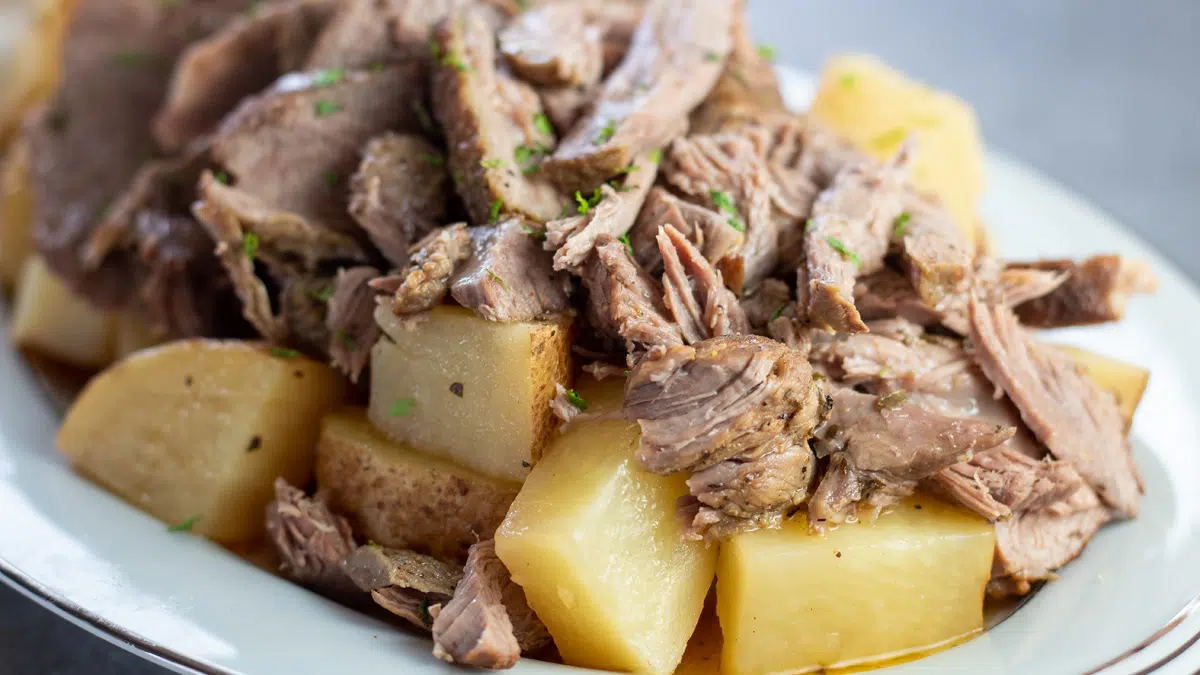 Wide image of slow cooker boneless leg of lamb on a white serving tray.