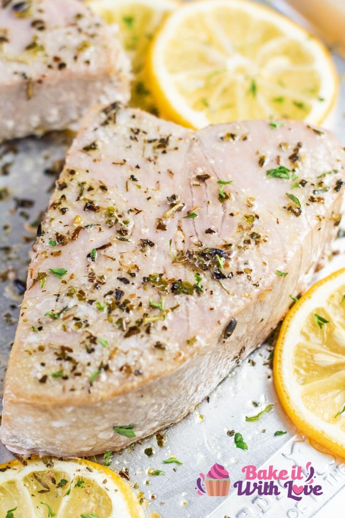 Closeup on the baked tuna steaks on sheetpan with seasoning and lemon slices.