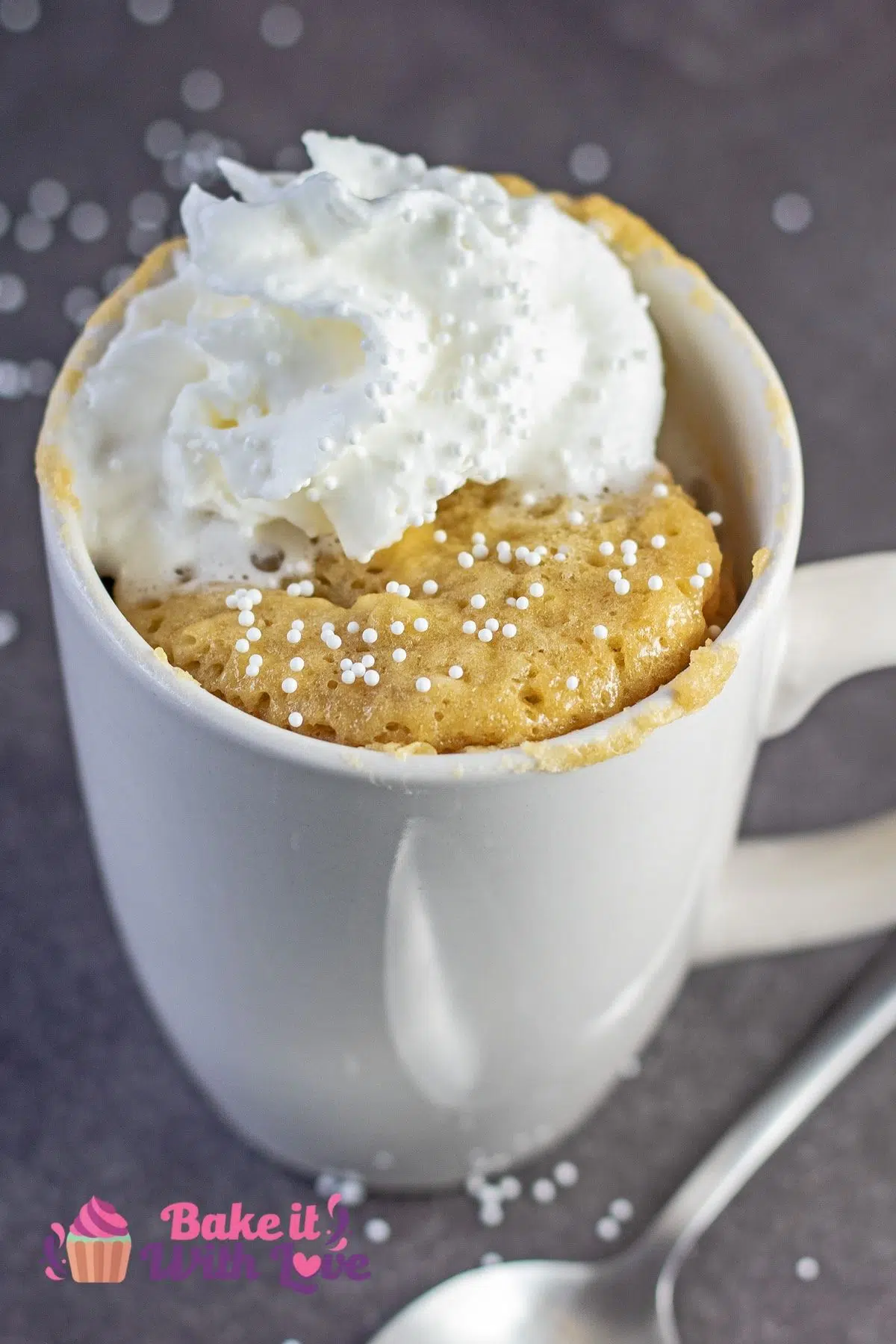 Best banana mug cake recipe served in white coffee mug and topped with whipped cream and white sprinkles.