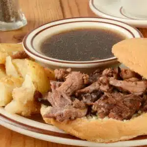 Best beef au jus served with steak sandwich on rimmed plate.