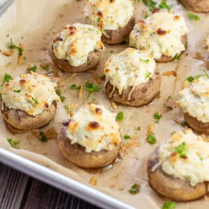 Closeup on the cream cheese stuffed mushrooms on baking sheet garnished with parsley.