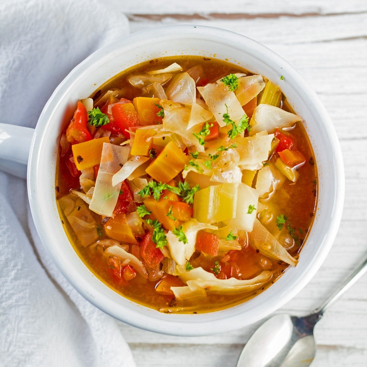 Best easy to make detox cabbage soup recipe loaded with vegetables in savory broth served in white bowl.