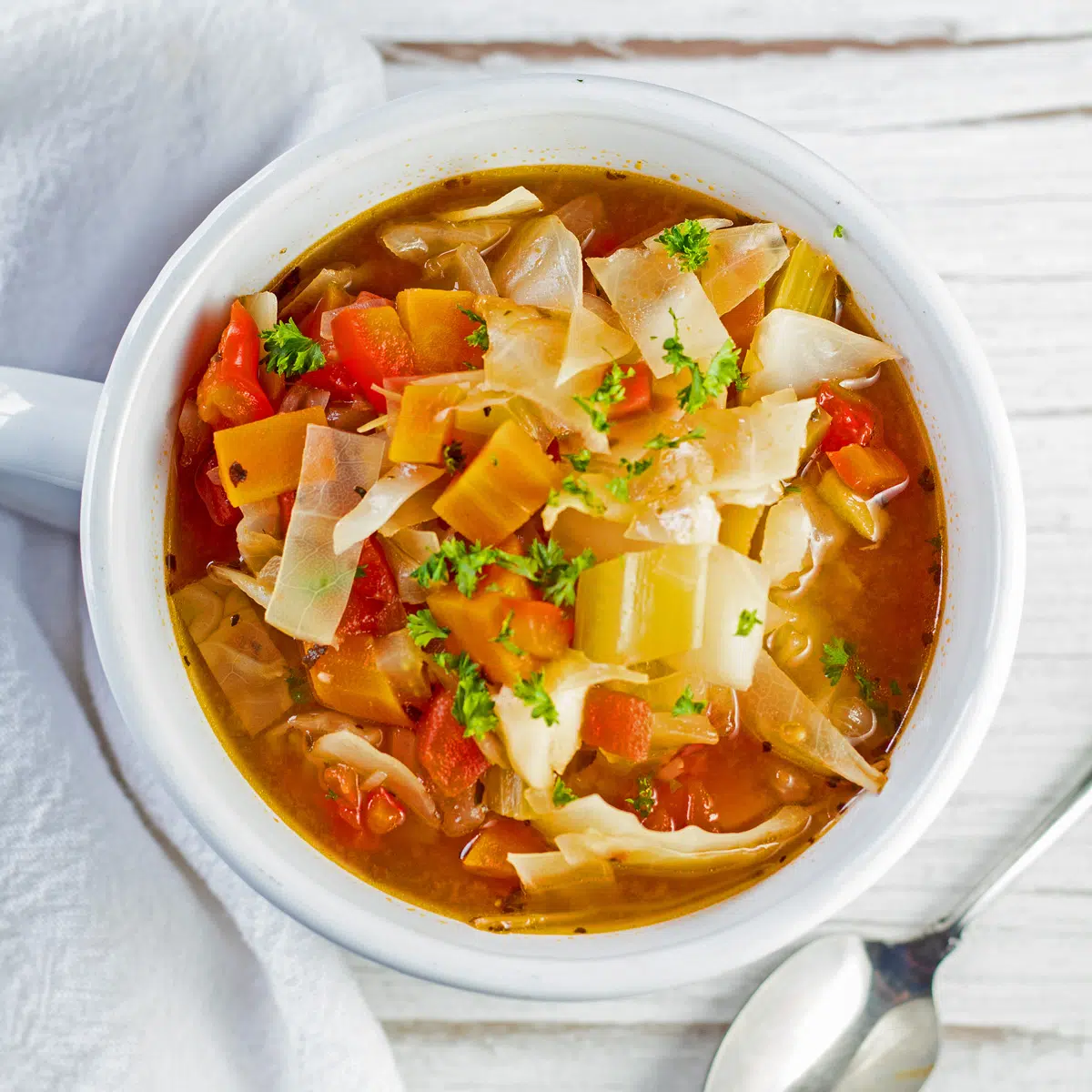 Best easy to make detox cabbage soup recipe loaded with vegetables in savory broth served in white bowl.