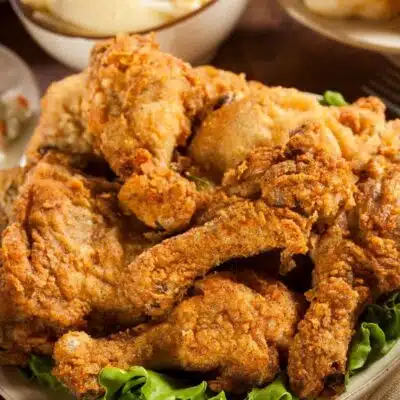 Easy classic fried chicken served on lettuce greens with sides in the background.