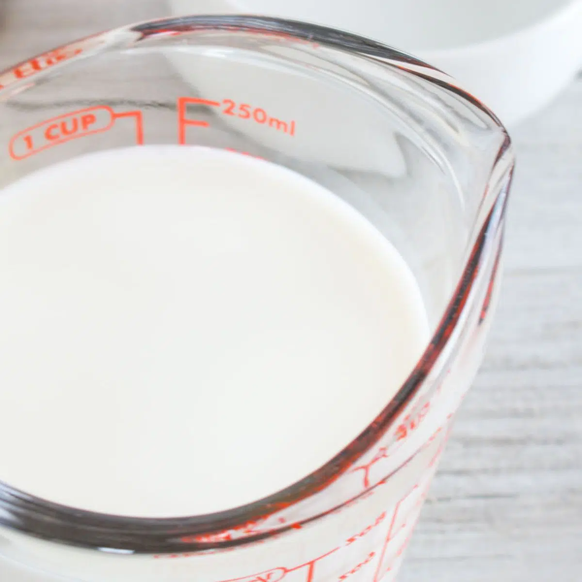 Square heavy cream substitute showing closeup on heavy cream in pyrex liquid measuring cup.
