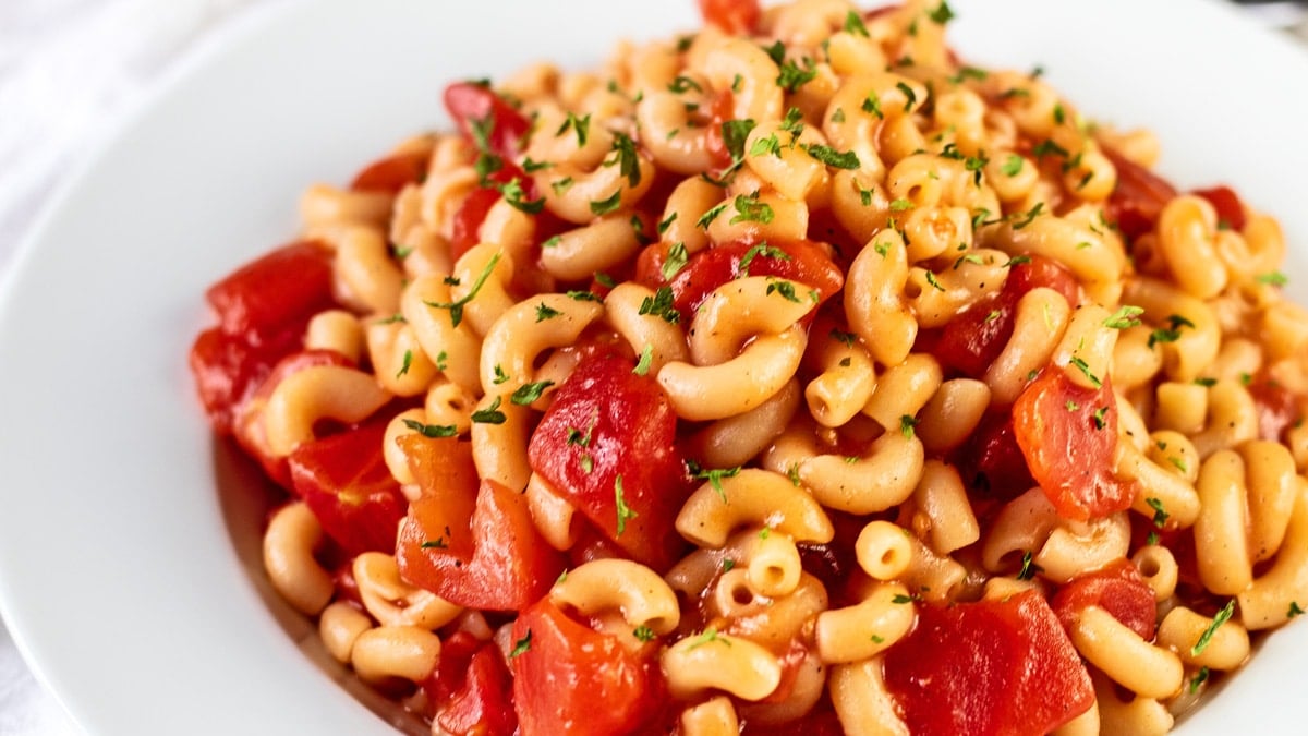 Breed beeld van macaroni en tomaten in witte pastakom.