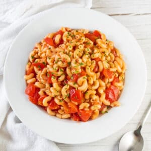 Tasty macaroni and tomatoes served in white pasta bowl on light background.