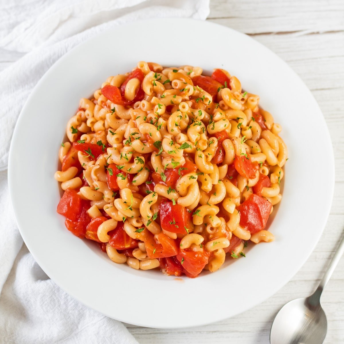 Tasty macaroni and tomatoes served in white pasta bowl on light background.