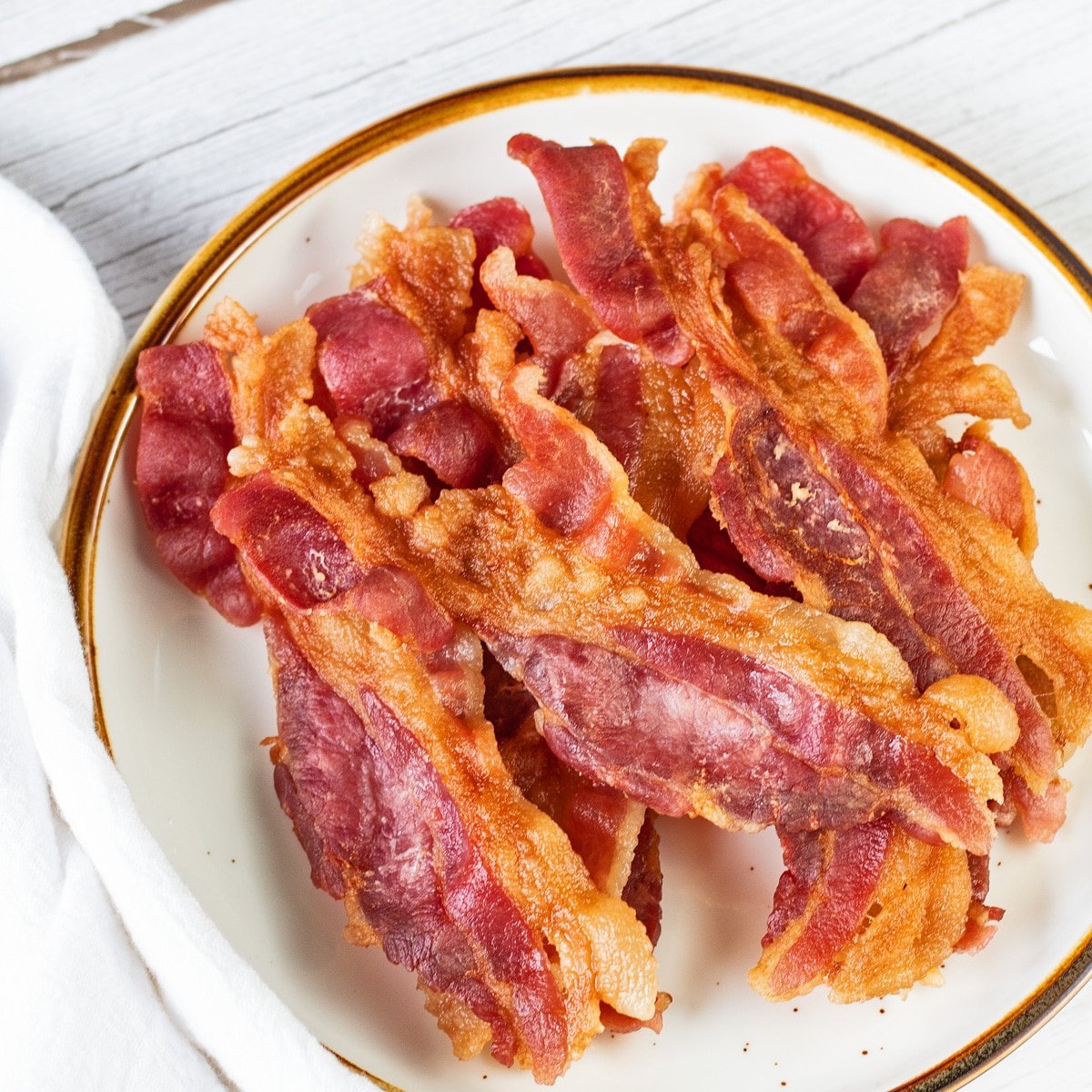 Bacon de micro-ondas servido em prato de borda marrom, cerca de 8 fatias empilhadas depois de crocantes com perfeição.
