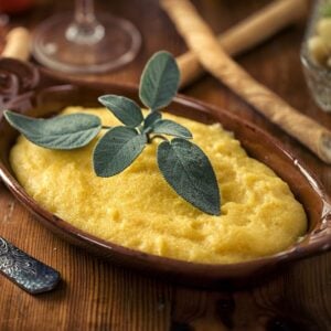 Easy creamy homemade polenta in brown serving dish with sage.
