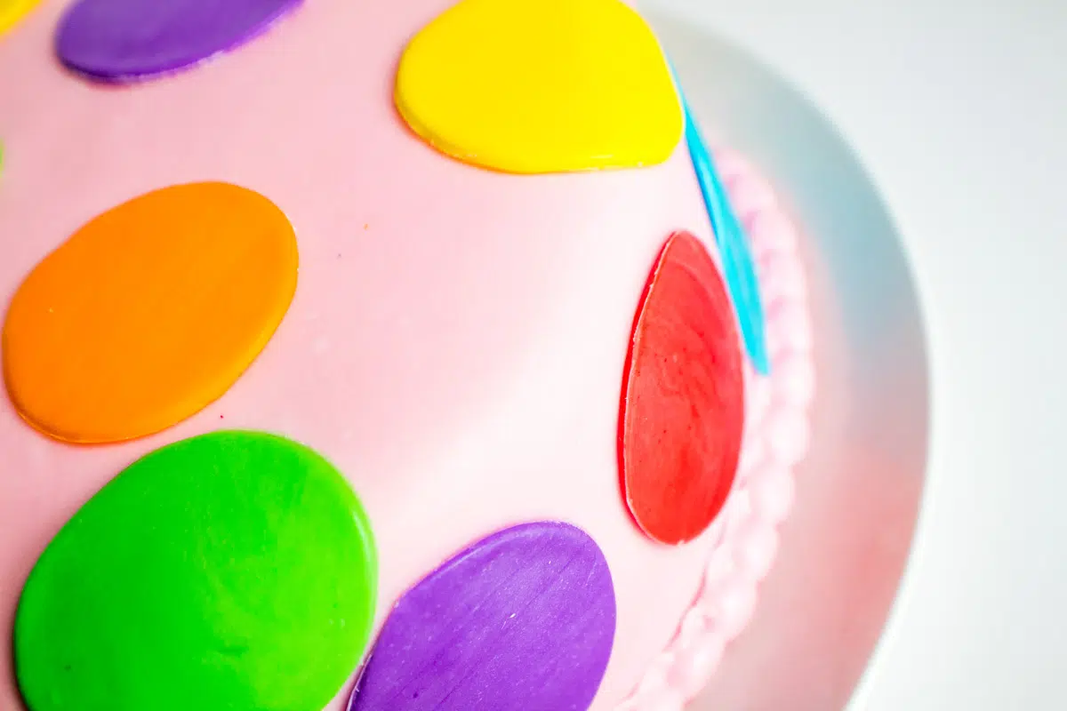 Horizontal image of rainbow layer cake with fondant polka dots.
