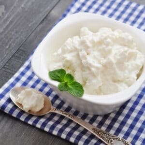 Meilleur substitut de fromage ricotta avec ricotta dans un bol blanc sur une serviette à carreaux bleus.