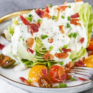 Closeup of the wedge salad on light grey plate and served with dressing, tomatoes, and bacon.
