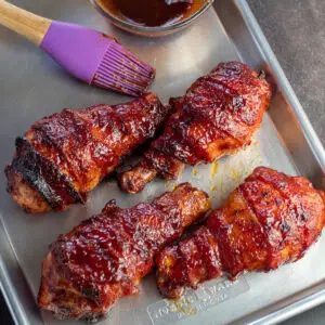 Square image of bacon wrapped bbq chicken drumsticks.