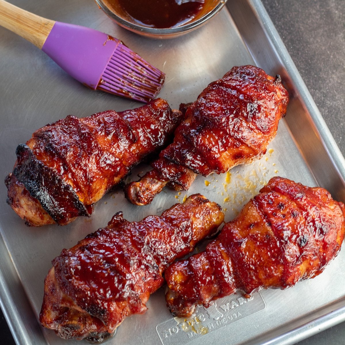 Image carrée de pilons de poulet barbecue enveloppés de bacon.
