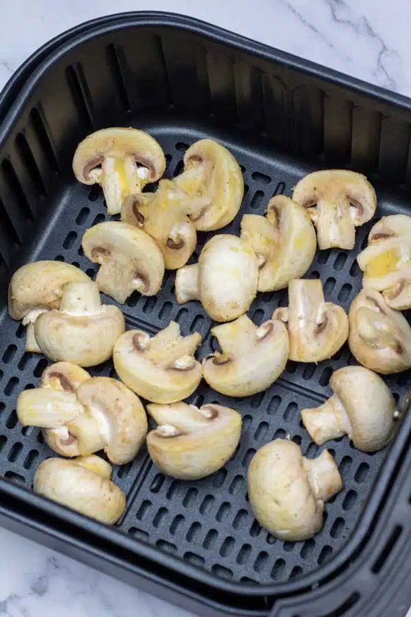Process photo 2 showing halved mushrooms in the air fryer basket before air frying.
