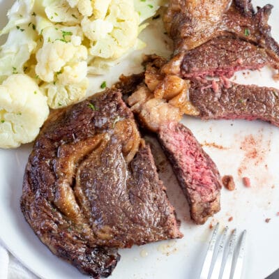 Potong steak penggorengan udara di piring putih dengan kembang kol di latar belakang.