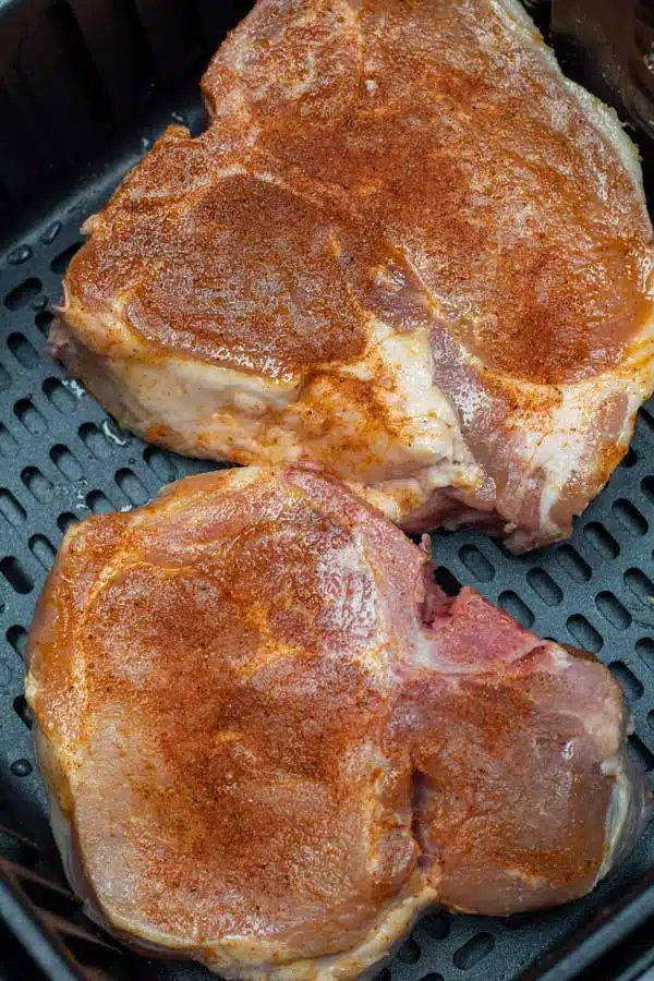 Process photo 1 seasoned thick cut pork chops in the air fryer basket.