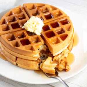 Image carrée de gaufres bisquick sur une assiette blanche avec du beurre et du sirop sur le dessus.