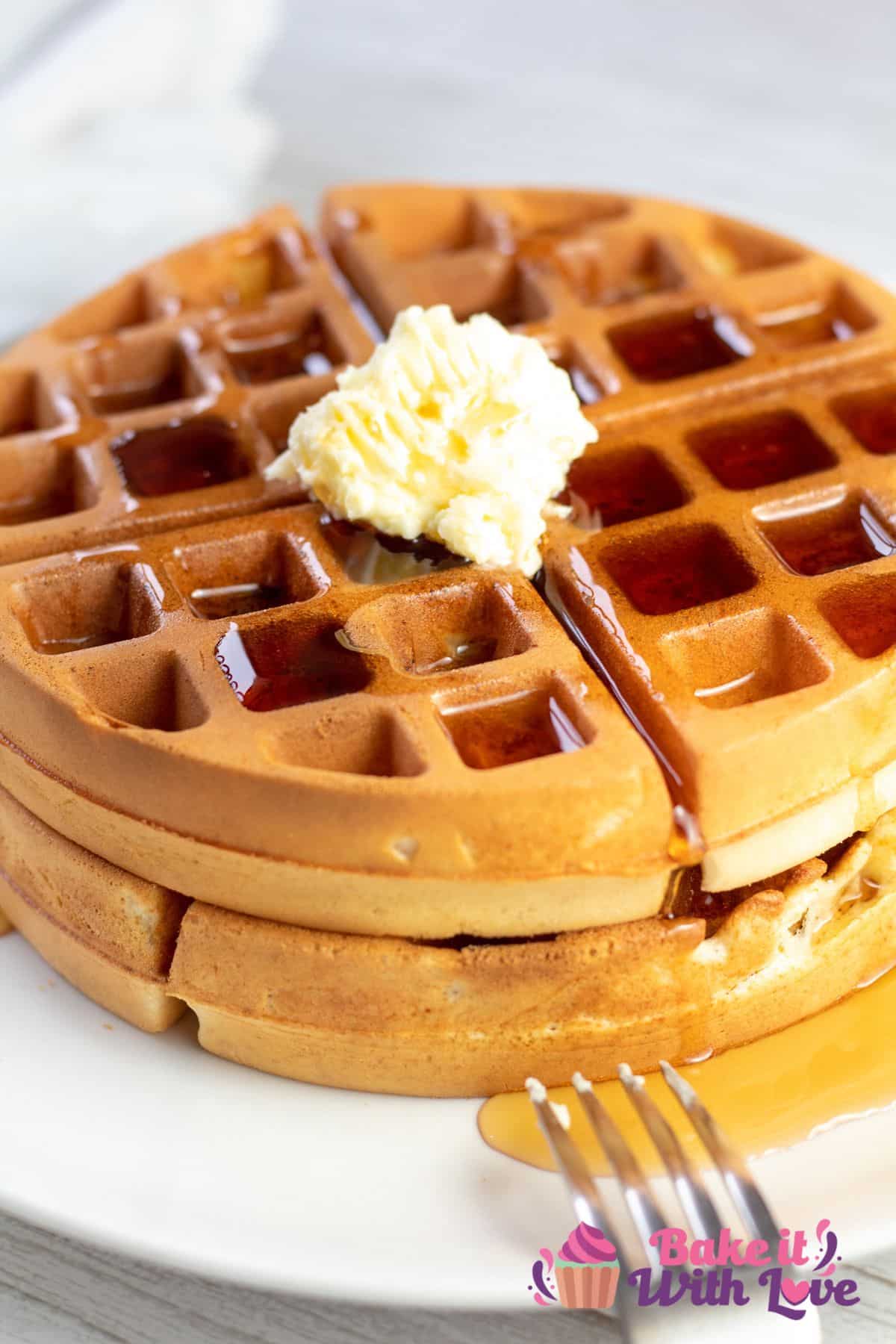 Tall image of bisquick waffles on a white plate with butter and syrup on top.